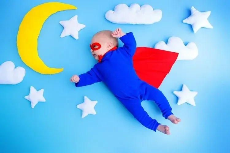 A newborn baby dressed as superhero lying between the stars and moon