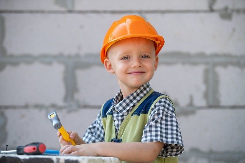 Cute little kid in builder helmet with repair tools on construction site