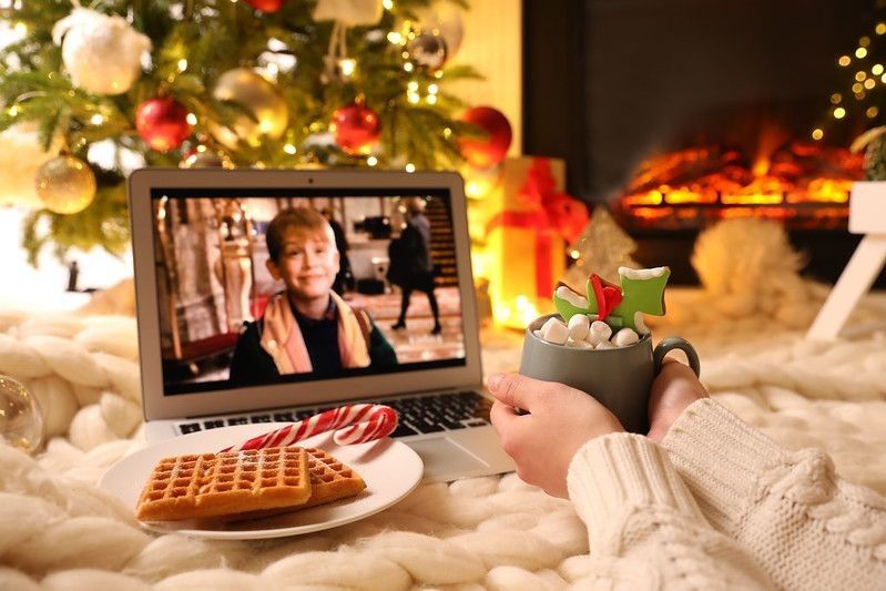 Woman with sweet drink watching Home Alone movie on laptop at home