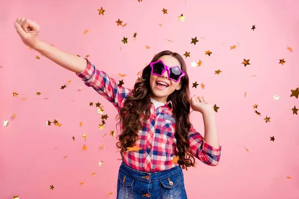 girl wearing star-shaped sunglasses showered with gold star confetti