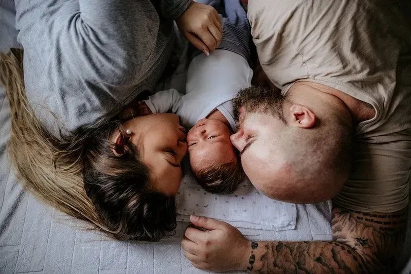 Parents lying on the bed either side of their newborn baby boy.
