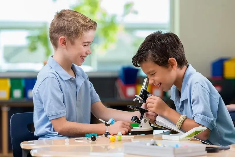 Two boys in blue shirts looking though a microscope and smiling.