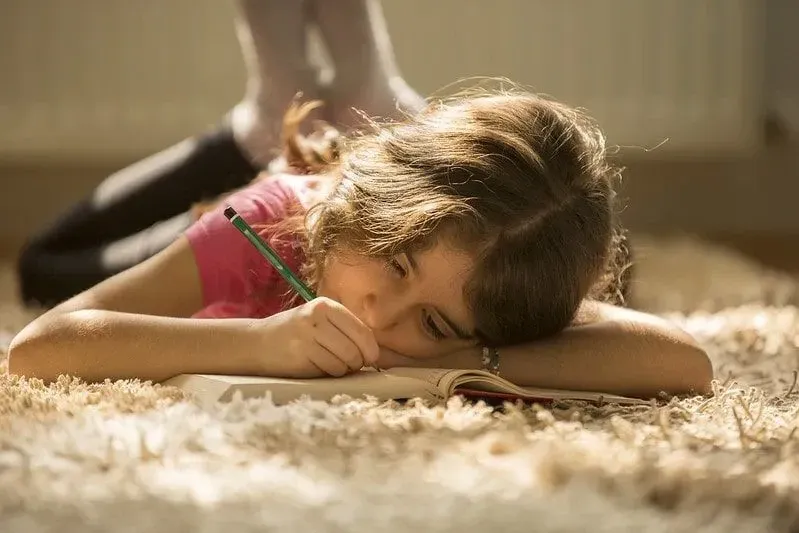 Little girl lying on the floor writing in her workbook.