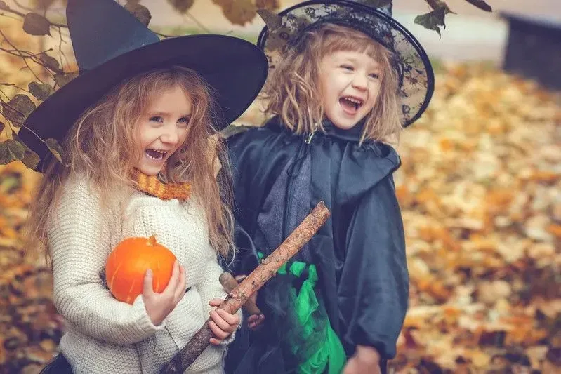 Two girls dressed as witches having fun in the Autumn leaves.