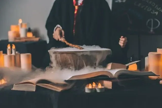 Wizard with their wand over a steaming cauldron. Surrounded by candles and a blackboard with spells in the background. 