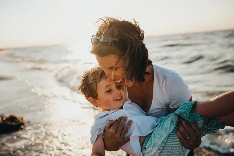 Mum carrying her son on the beach, both laughing and happy.
