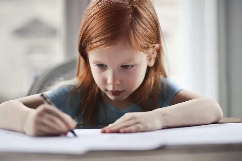 Young girl with red hair writing spelling on paper.
