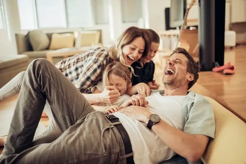 Family of four falling back on the sofa laughing at parrot jokes.