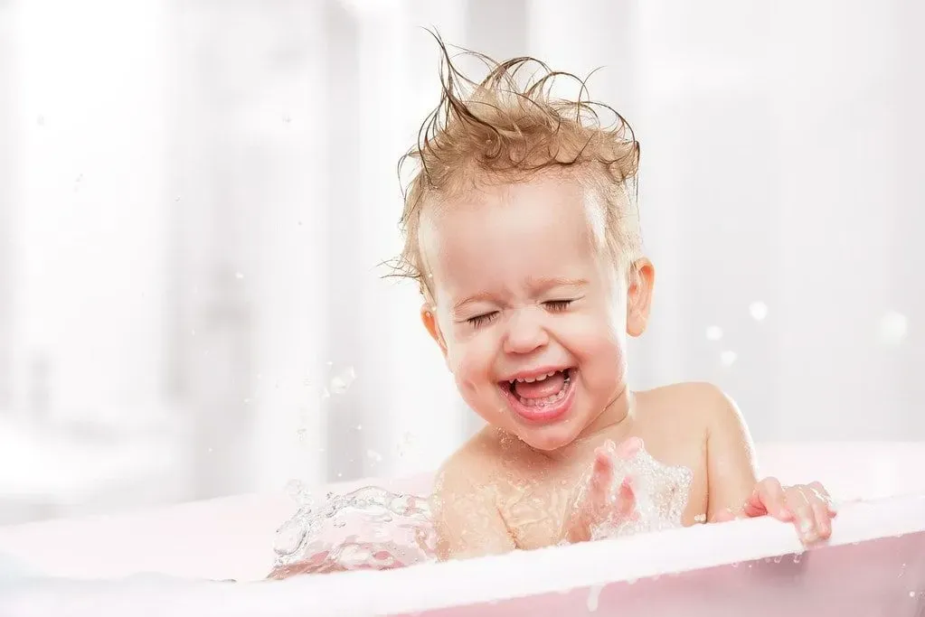 Happy baby having her hair washed in the bath tub.