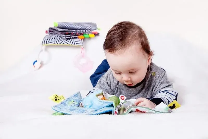 A baby boy is laying on the floor, playing with a soft book.
