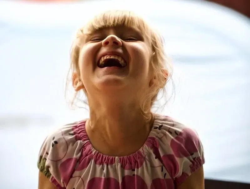 Young girl with a fringe throwing her head back in laughter.