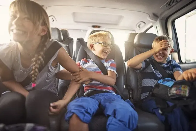Three kids sitting in the back of the car laughing.