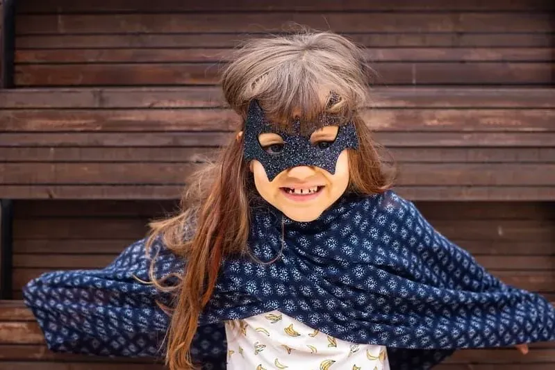 Little girl wearing a glittery bat mask and a makeshift cloak.