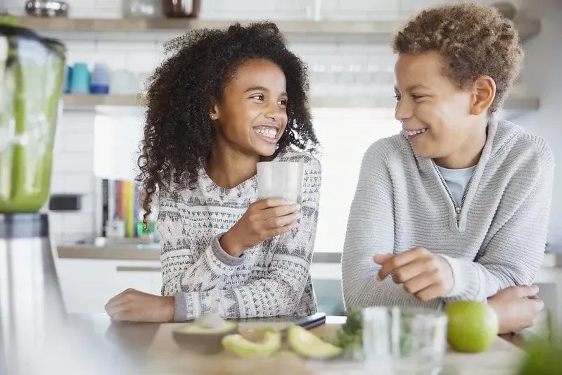 Girl and boy laughing together enjoying an avocado smoothie.