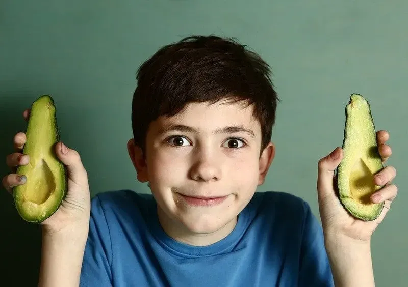 Young boy holding half an avocado in each hand making a silly face.