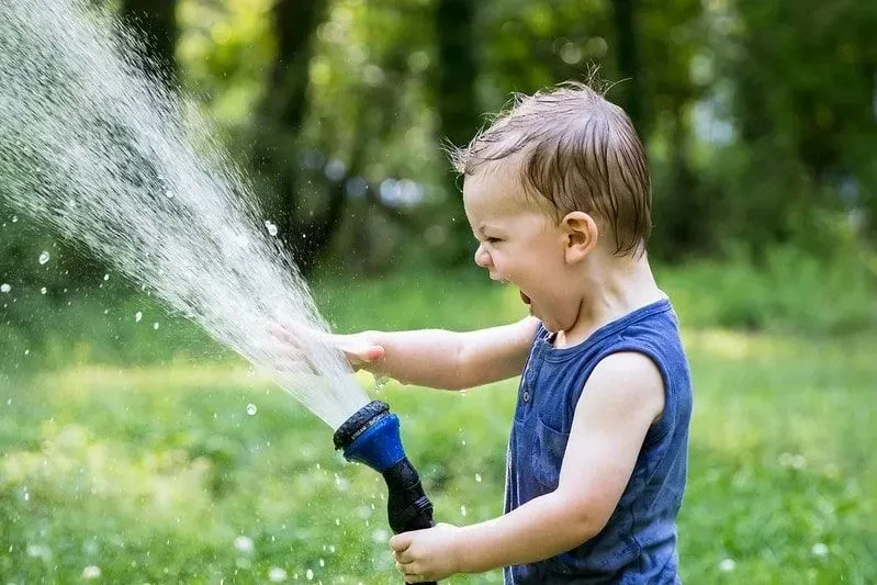 Young boy laughing while spraying water out of the hose.