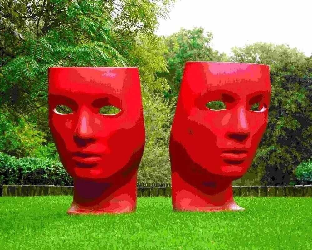 large sculpture of two red faces in a park
