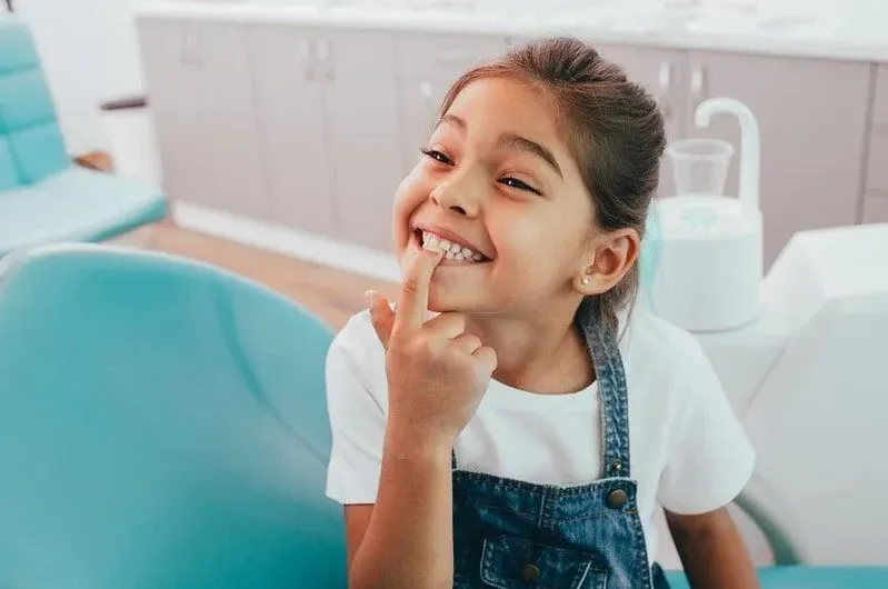 Little girl at dentist smiling and pointing to her teeth.