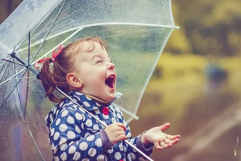 Little girl in fits of laughter as she stands under her umbrella in the rain.