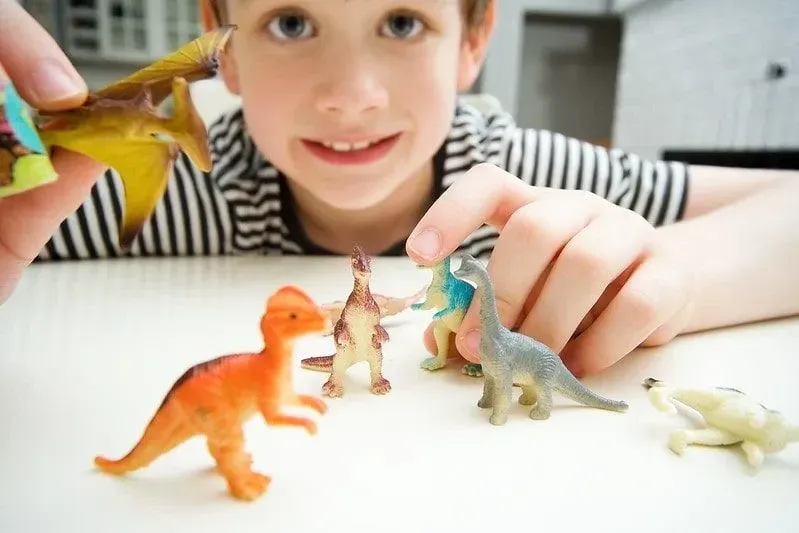 Young boy sat at the table playing with little toy dinosaurs.