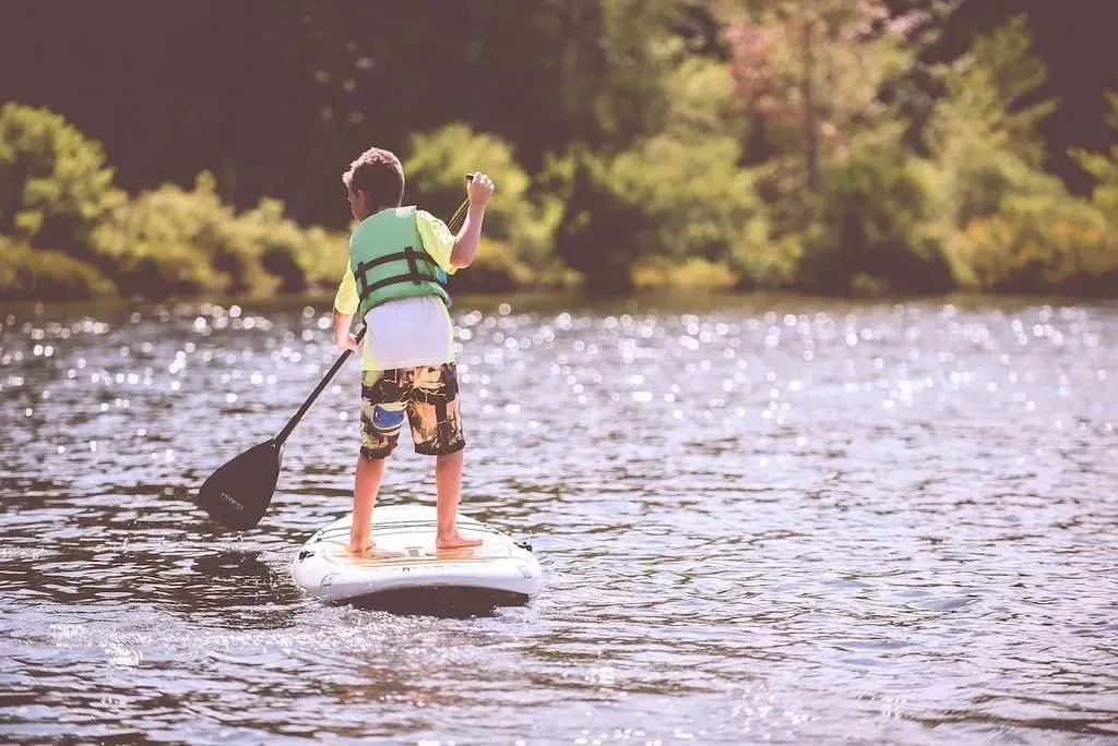 Young boy paddle boarding on a lake surrounded by trees.