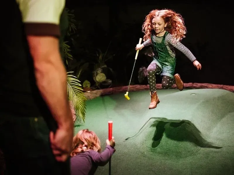 Little girl leaping over the adventure golf course holding a golf club.