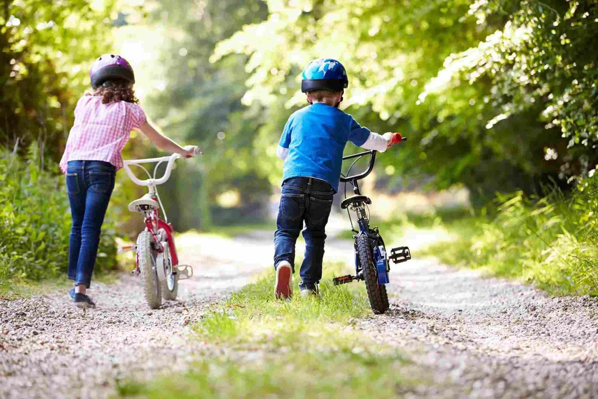 children in helmets pushing bikes along a path