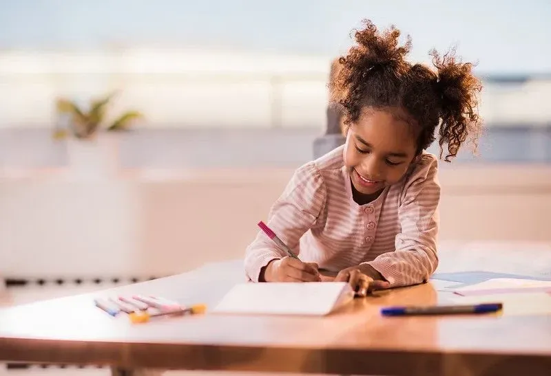 Girl relaxing on the table at home and coloring in notebook