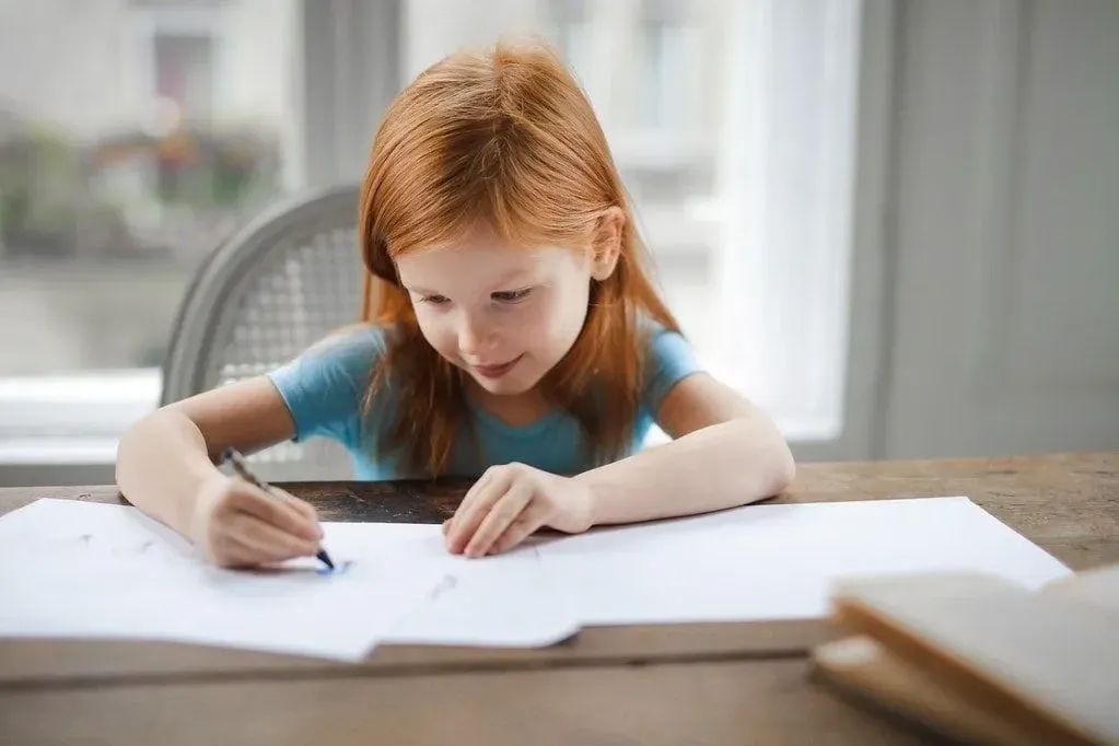 Young girl sat at the table drawing on some pieces of paper.
