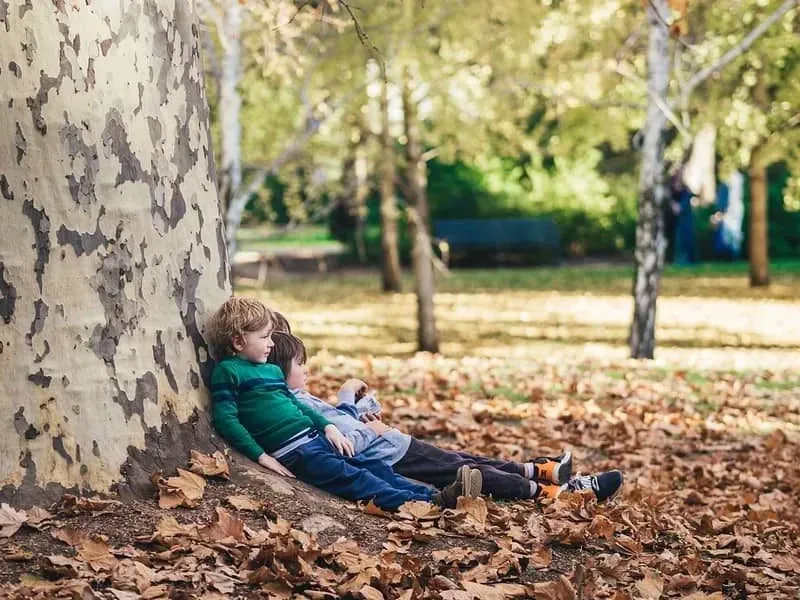 Little boys sat relaxing against a tree, enjoying being outdoors in nature.