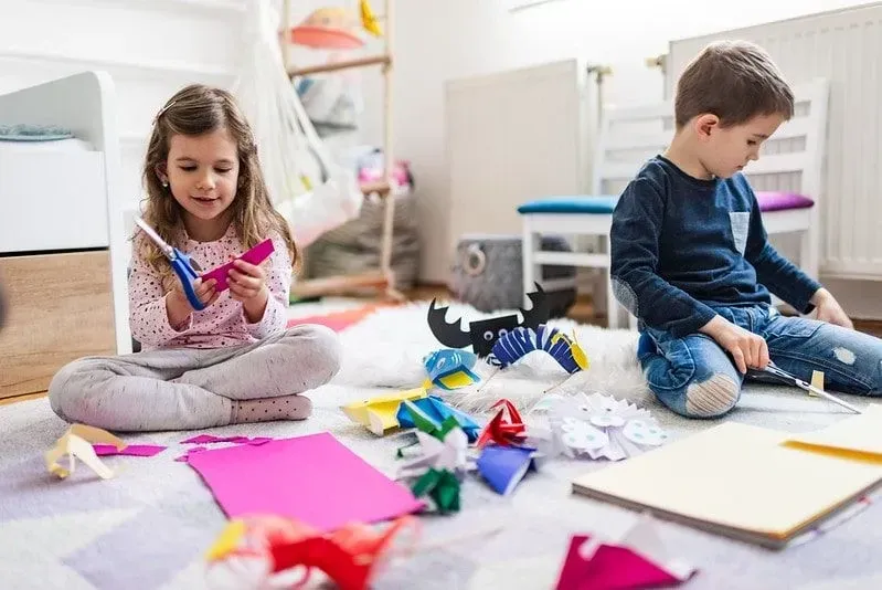 Little boy and girl sat on the floor cutting paper and doing origami.
