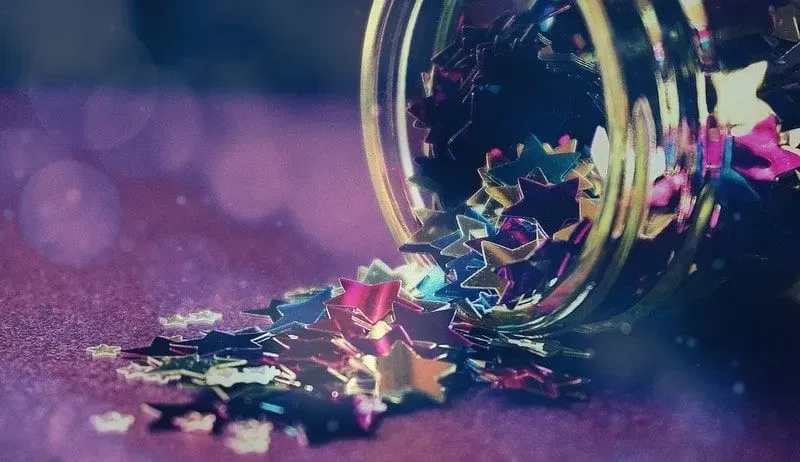 Coloured, shiny star sequins tipping out of a jar onto a surface.