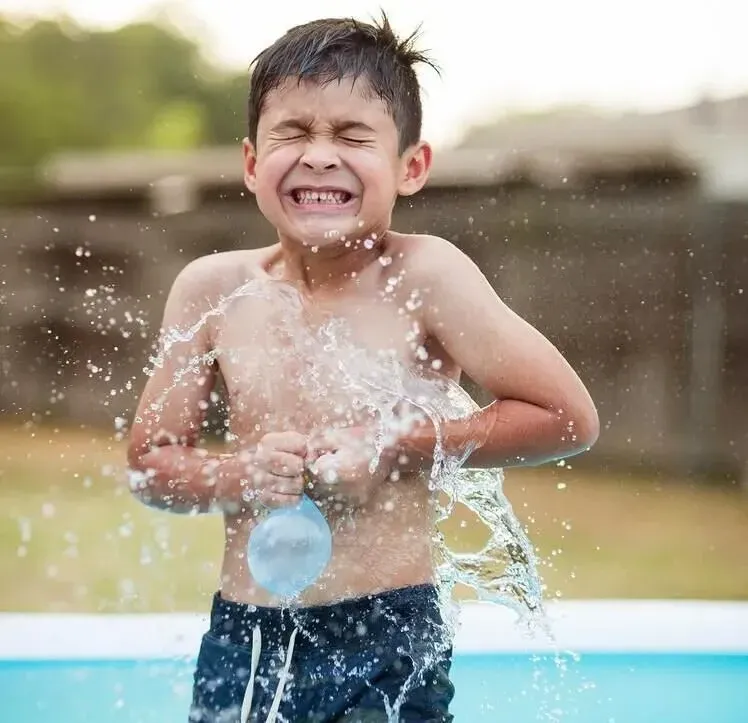 Young boy in a paddling pool in the garden getting splashed by a bursting water balloon.