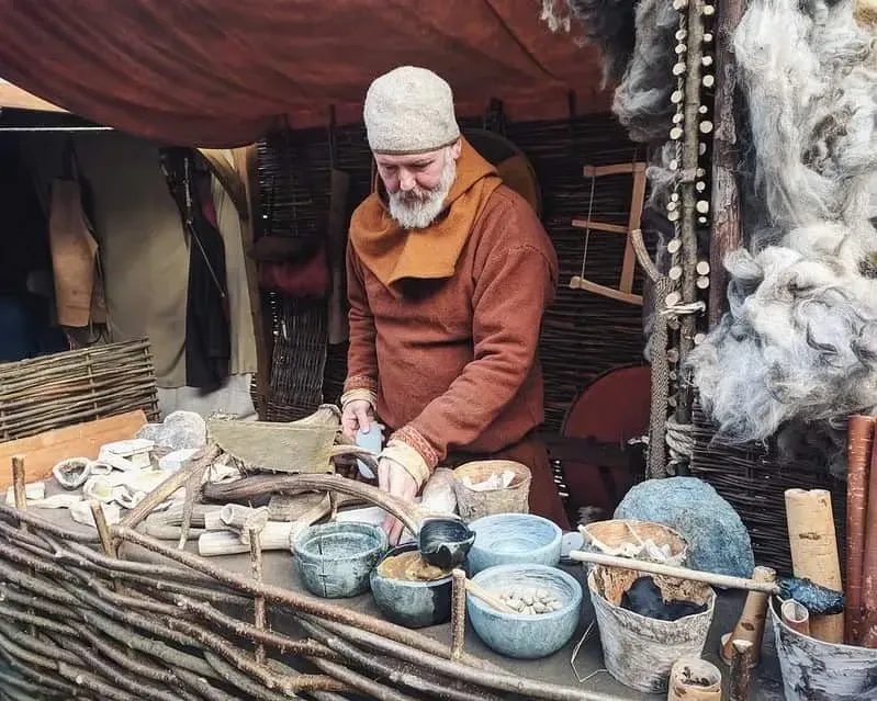 Man wearing Viking clothing, standing behind a stall making Viking pots and horns.