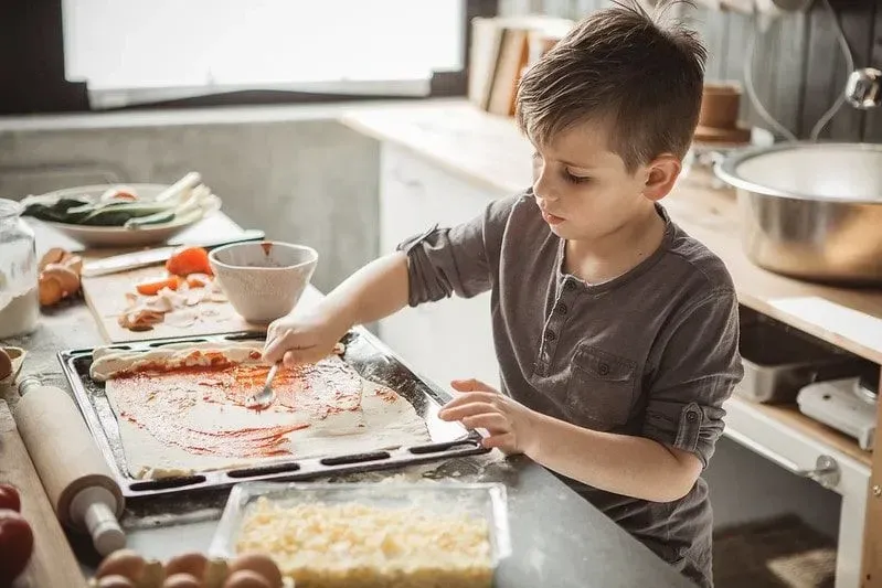 Young boy in the kitchen making homemade pizza.