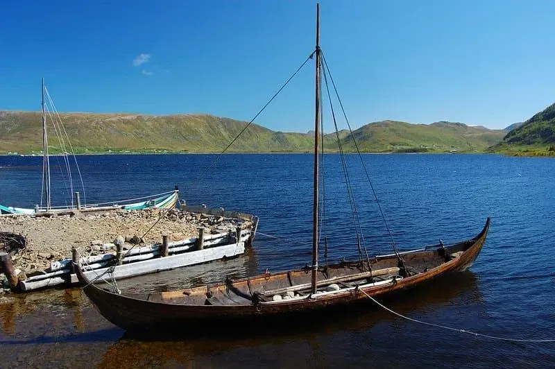 A Viking longship on water surrounded by hills and with a blue sky.