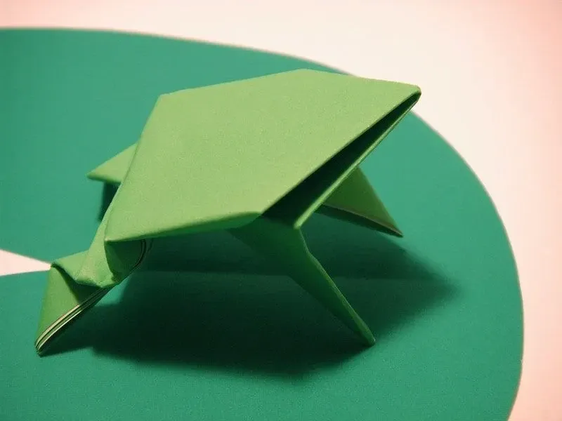 Green origami frog on a green paper lily pad.