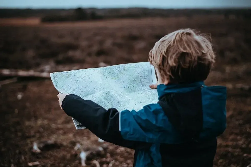 Young boy holding up a map reading it in the countryside.