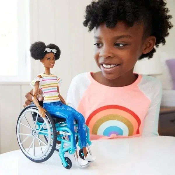 Young girl playing with her Barbie fashionista doll in a wheelchair.