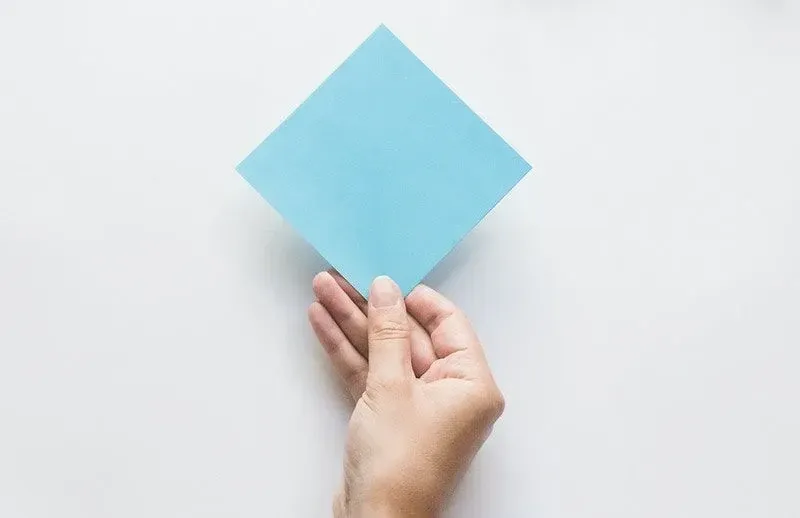 Hand holding a square of blue origami paper.
