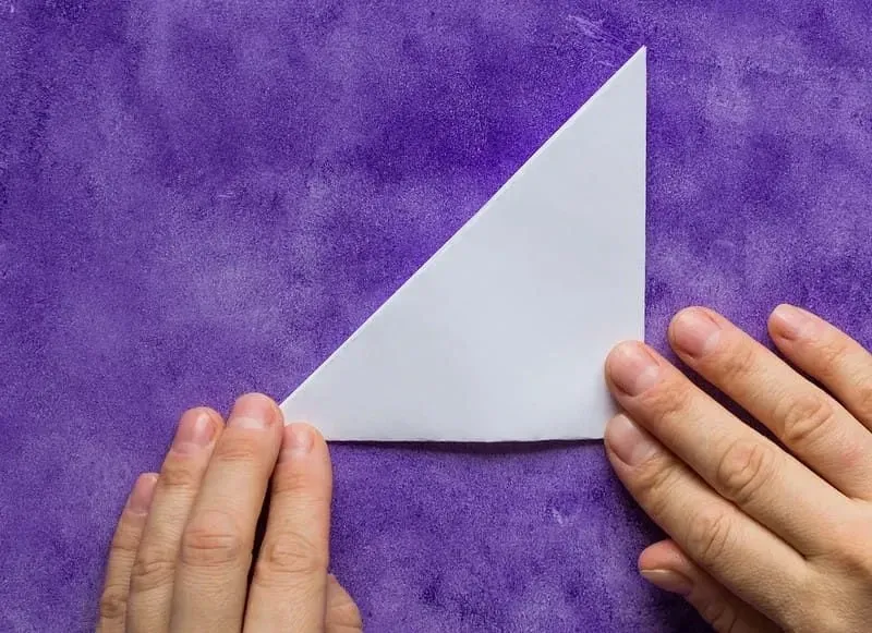 Piece of origami paper folded in half diagonally, hands pressing it down.