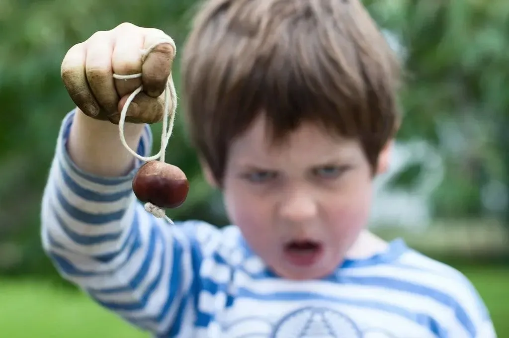 Young boy with soil all over his hands holding up a conker and making a silly face.
