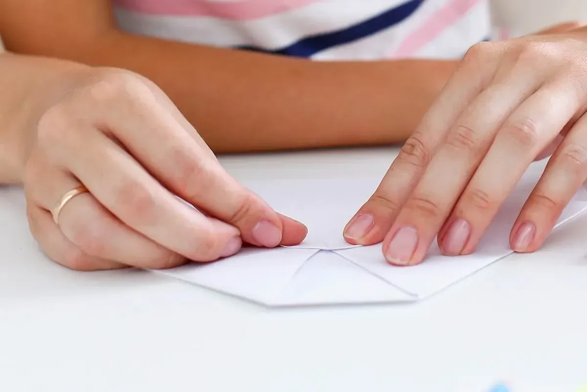 Close up of hands folding a white piece of paper to make an origami squirrel.