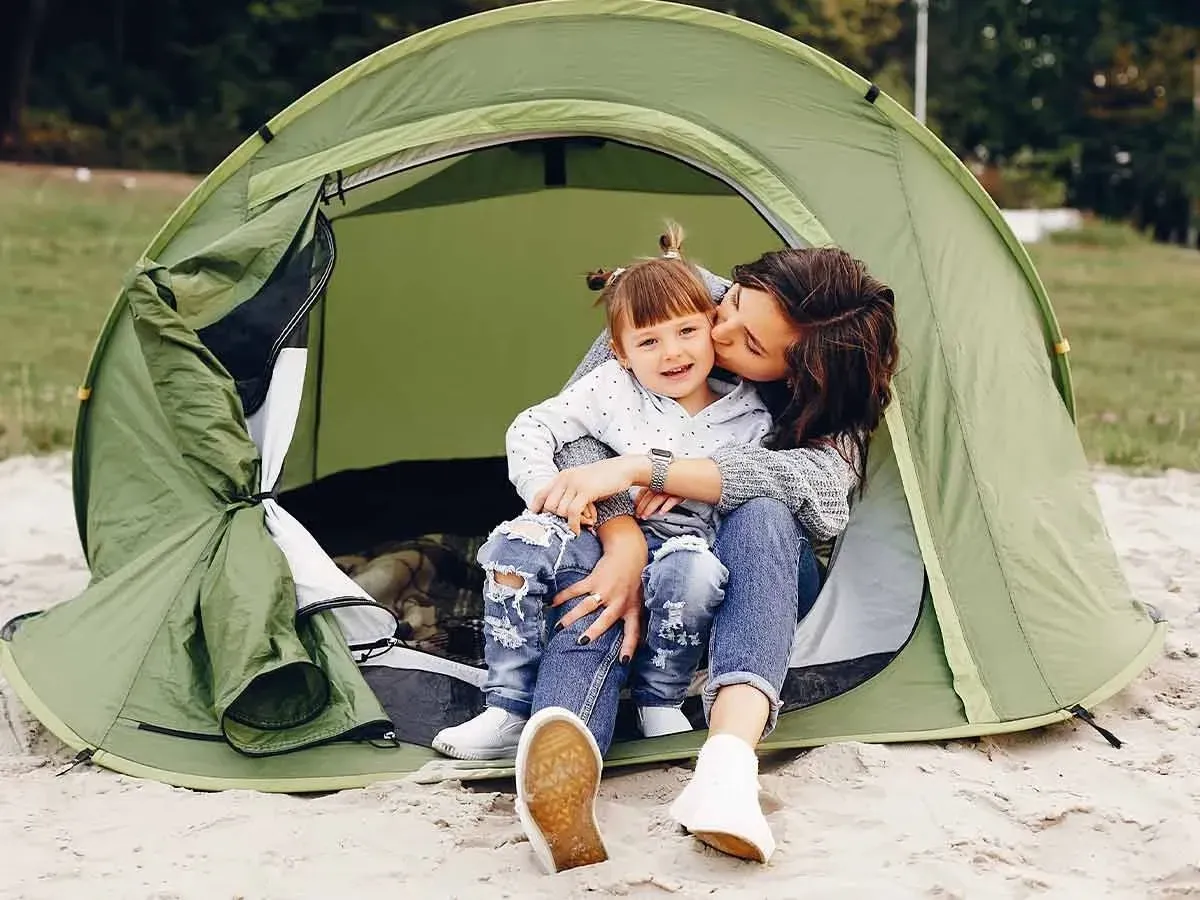 Mum kissing her toddler on the cheek while they sit in their tent on a camping holiday.