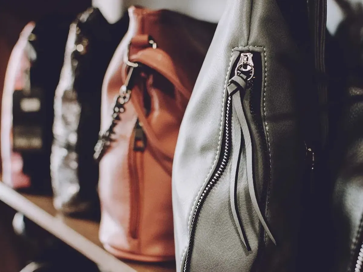 A close up image of four leather bags of different colours sitting on a shelf.