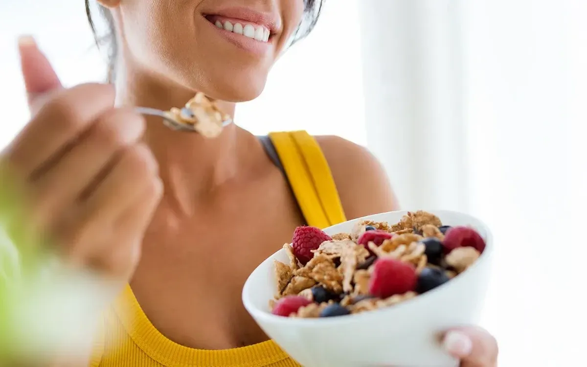 A close up image of a woman smiling as she eats a bowl of cereal representing the beginning of the digestive system.