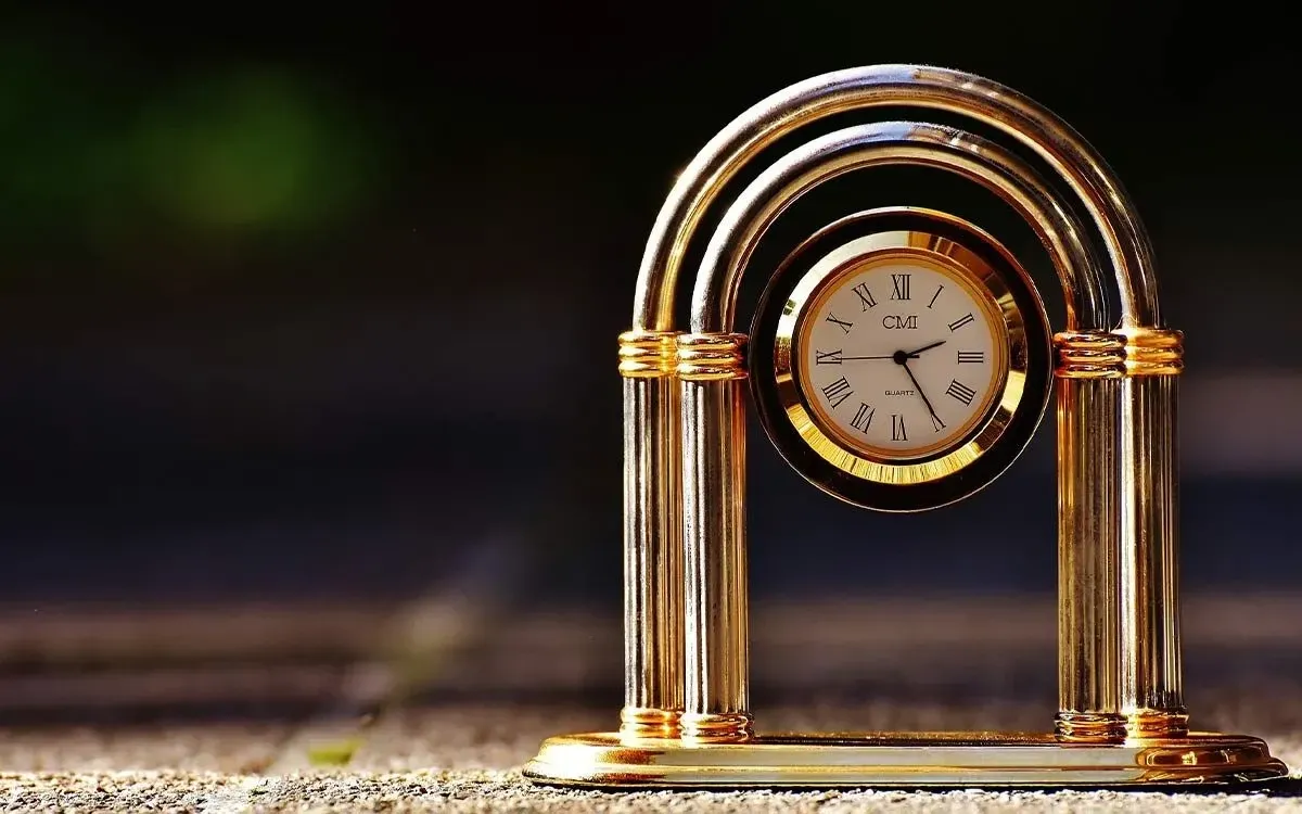 An image of a small gold clock which uses Roman numerals.