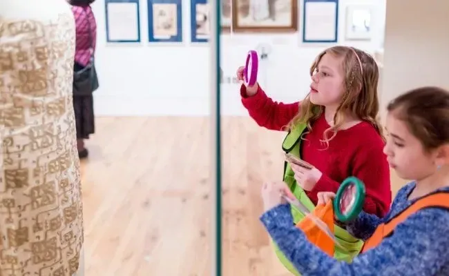 Two kids examining a museum display with a magnifying glass.