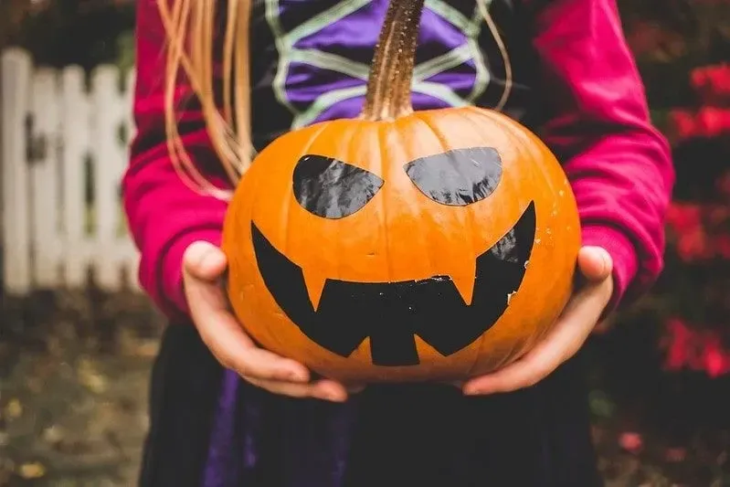 Girl holding a Halloween pumpkin with a scary face on it.