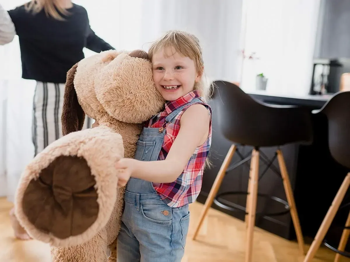 Little girl hugging a giant dog shaped soft toy.